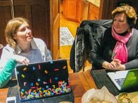 Two teachers are sitting at a table with their laptops out.