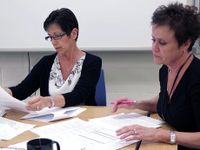 Two teachers working side-by-side at a table covered with papers