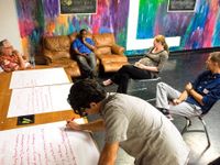 Five teachers in the lounge in discussion while one takes notes