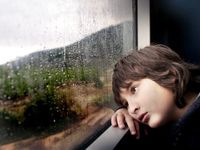Boy leaning his head against a window sill looking out at the rain
