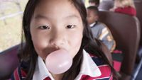 A young girl chews gum on a school bus.