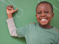 A photo of an elementary-school boy in front of a green chalkboard, smiling.