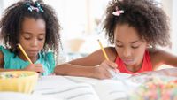Two girls work on their homework side by side.