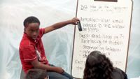 Boy sitting in front of a white board instructing the class
