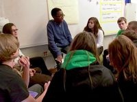 Boy on stool teaching engaged classmates circled around him
