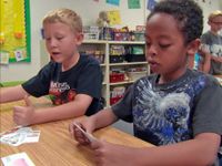 Two boys at a table looking at cards printed with various items to determine want versus need