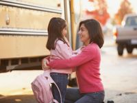 A photo of a parent and child in front of a school bus.