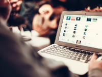 A photo of an adult on a laptop, with icons to various apps on the screen.