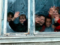 A photo of a group of elementary students looking out a window, waving and smiling.