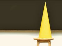 Yellow dunce cap sitting on a stool in front of a blackboard