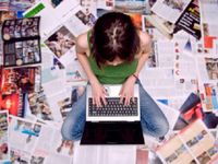 A photo of a female high school student working on a laptop, surrounding by articles.