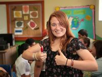 Girl in a classroom standing in front of students working giving two thumbs up