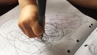 A child’s hand scribbling in pen in a lined notebook