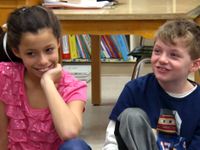 Girl and boy sitting on floor as part of circle, smiling