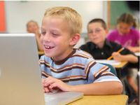 Boy at his desk laughing at something on his laptop