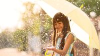 Young girl smiling and holding an umbrella, with hand extended touching raindrops.