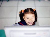 Young girl laughing in front of computer monitor