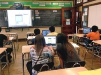 Students in class working in pairs on laptops looking at a projection on screen