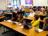 A classroom full of teachers listening with laptops open