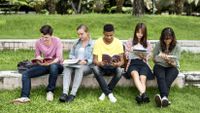 A group of students sit outside taking notes on what they notice about the world around them.
