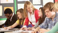 A teacher checks in with one student as others write.