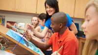 A teacher guides several high school aged students as they sit at easels, painting.