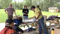 A group of people work on an electrical project at an outdoor picnic table.