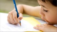 A young student is seen very close up writing on a sheet of paper with a pencil.
