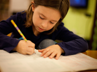 A photo of an elementary-school girl writing in her notebook with a pencil.