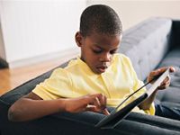 Boy sitting at end of a couch working on a tablet