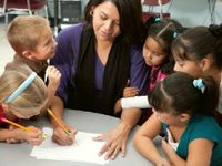 Teacher writing with a pencil surrounded by five young engaged students