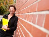 Woman leaning against brick building holding a yellow folder