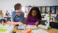 A young boy and girl work together with a microscope and an iPad.