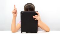 A girl hidden behind a tablet computer raises her hand.