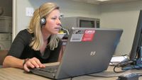 Woman wearing a headset sitting at her kitchen table with her laptop