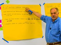 Man pointing to 21st Century Learning Experience notes on big yellow easel paper taped onto a whiteboard
