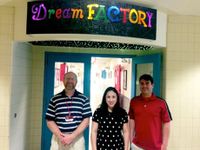 Three adults are standing outside of the doors of a school hallway, below a sign that says, "Dream Factory."