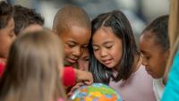 A diverse group of kids look at a globe together.