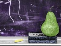 A photo of a pear on an eraser, on a chalkboard shelf.