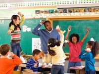 Male teacher scratching his head surrounded by students having a balled up paper fight