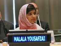 A young woman is sitting in front of two men, with a microphone by her mouth, and her name, Malala Yousafzai, displayed in front of her.