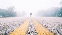 A student stands in the middle of a fog-shrouded road.