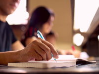 A photo of the arm and hand of a high school male, writing in his notebook.