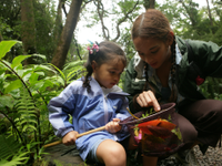 Older girl pointing at something in a net held by a younger girl in a forest