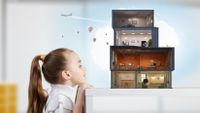 A young girl imagines that a pile of small boxes on a table are a house complete with electricity, with a plane and hot-air balloons flying above.