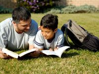 A man and boy reading on the lawn in the backyard