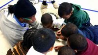 Teacher on the floor surrounded by working students