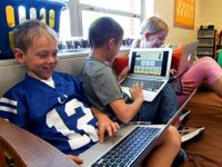 Three kids sitting in class on a big futon each with a laptop