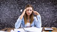 A stressed-out young woman sits in front of a blackboard crowded with numbers and equations.
