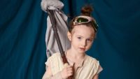 A young girl is dressed up in costume as Rey, the female protagonist from the movie Star Wars: The Force Awakens.